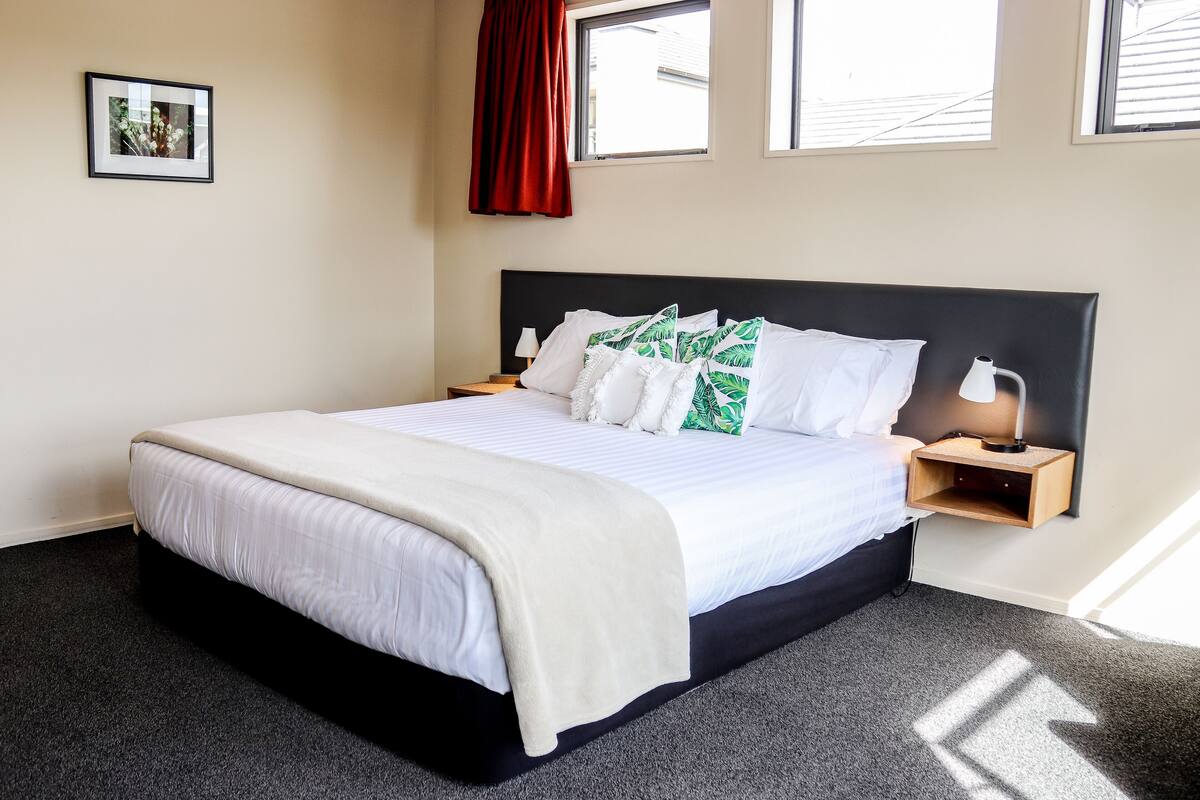 A neatly made bed with white bedding and green pillows, a bedside table with a lamp, and a framed picture on the wall.
