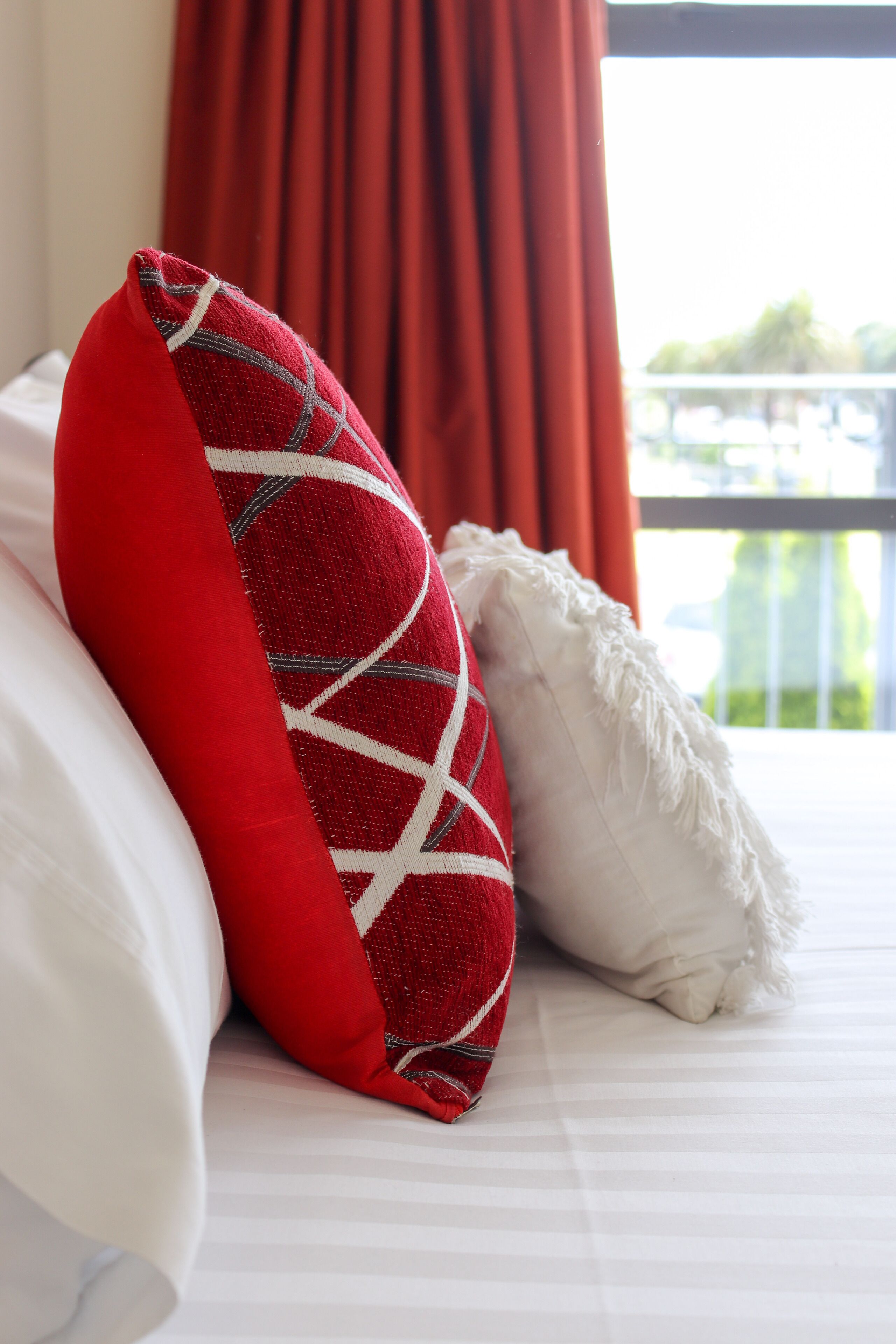 A bed with a red and white pillow, a white pillow, and a red curtain in the background.