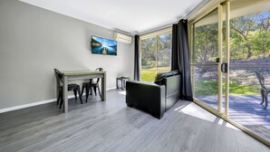 A modern living room with a dining area, a sofa, and a large sliding glass door leading to a deck.