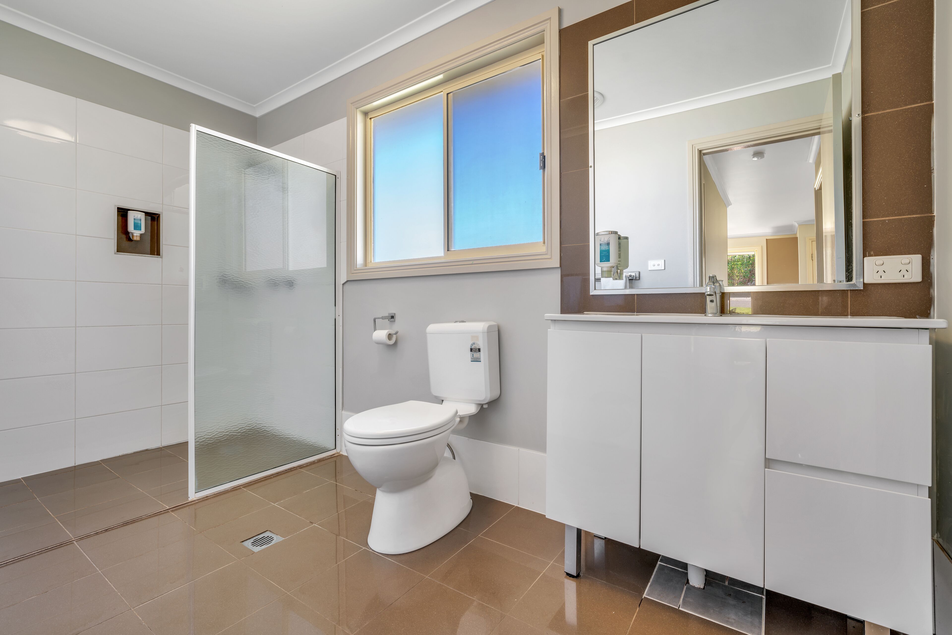 Een moderne badkamer met toilet, douche en wastafel met spiegel.