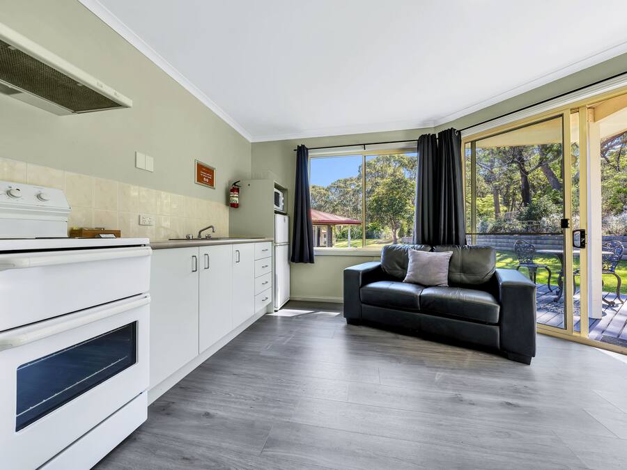 Une cuisine moderne équipée d’une cuisinière, d’un four et de placards, d’un canapé en cuir noir et d’une porte-fenêtre coulissante donnant sur une terrasse.
