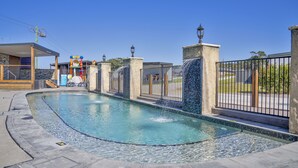 A swimming pool with a tiled edge, a water feature, and a fence.