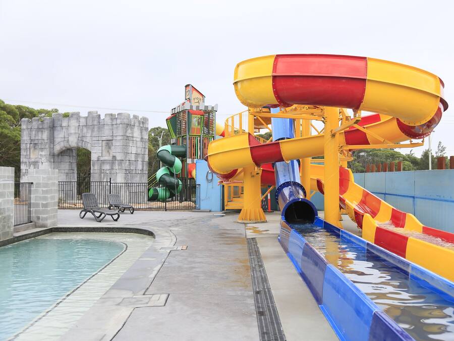 Un parque acuático con piscina, toboganes y una estructura con forma de castillo.
