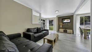A modern living room with a black leather sofa, a wooden coffee table, and a TV mounted on the wall.