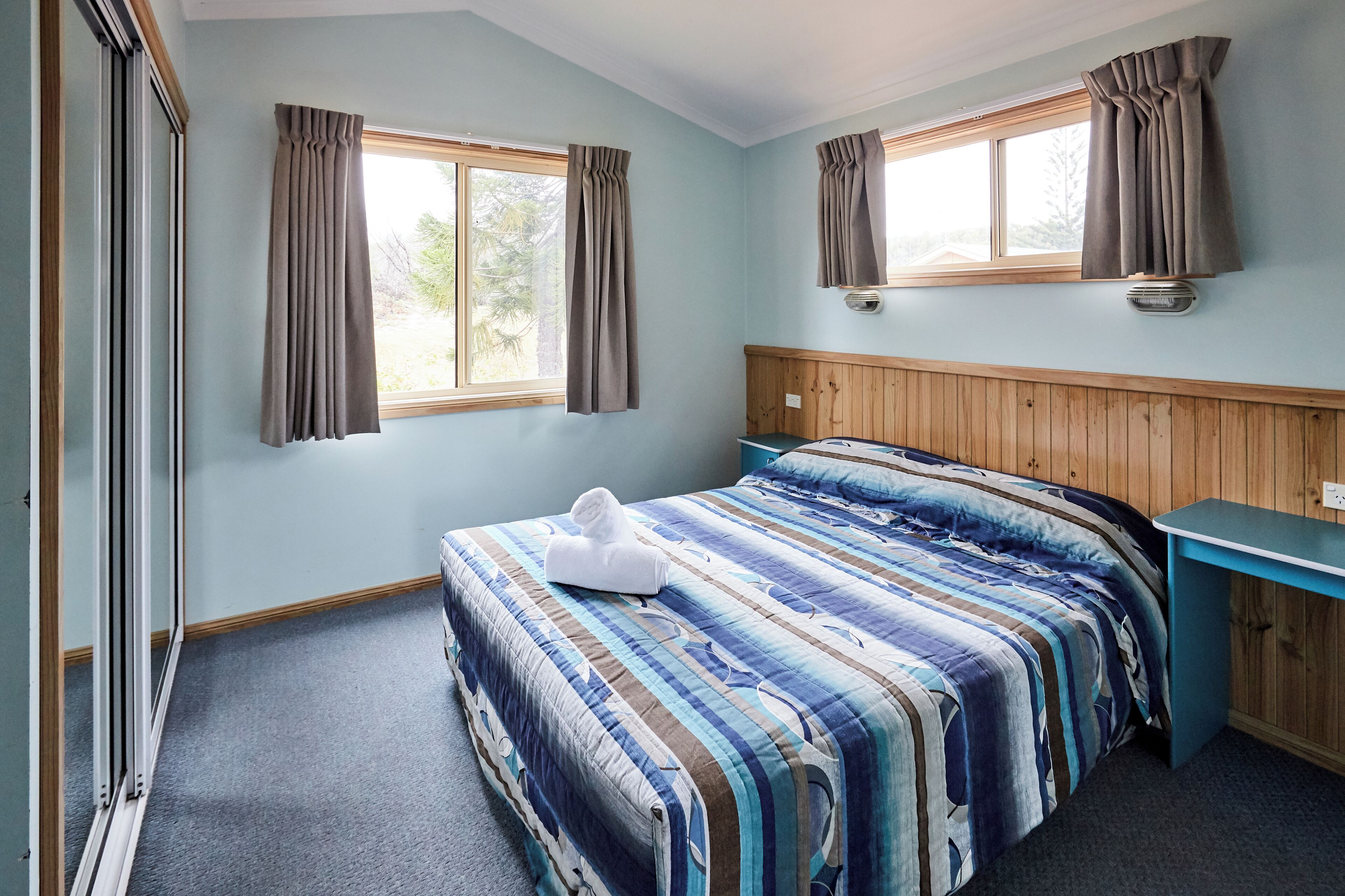 A bedroom with a bed, a wooden headboard, a window with curtains, and a small desk.