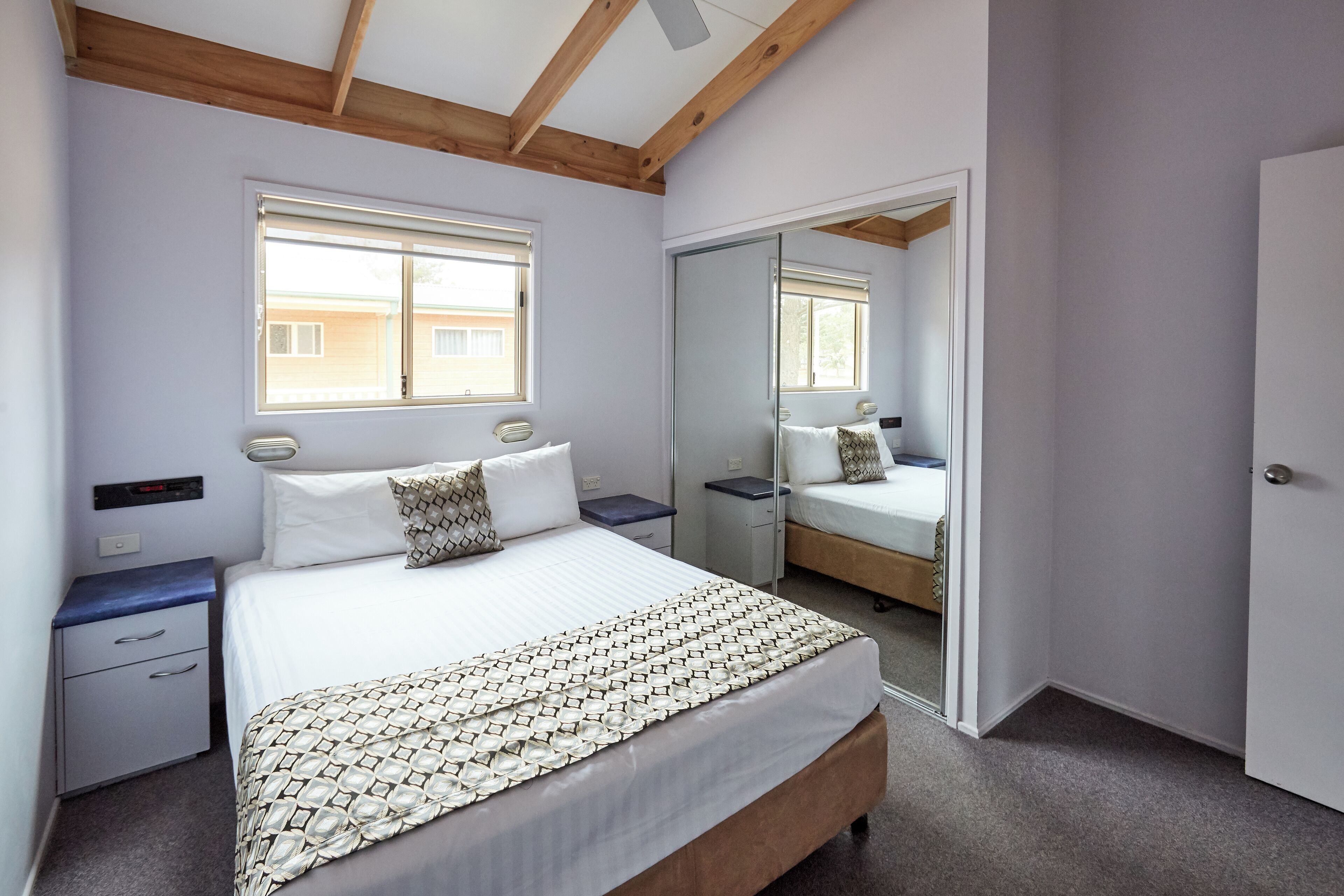 Une chambre à coucher avec un lit, des tables de chevet, un miroir et une fenêtre.