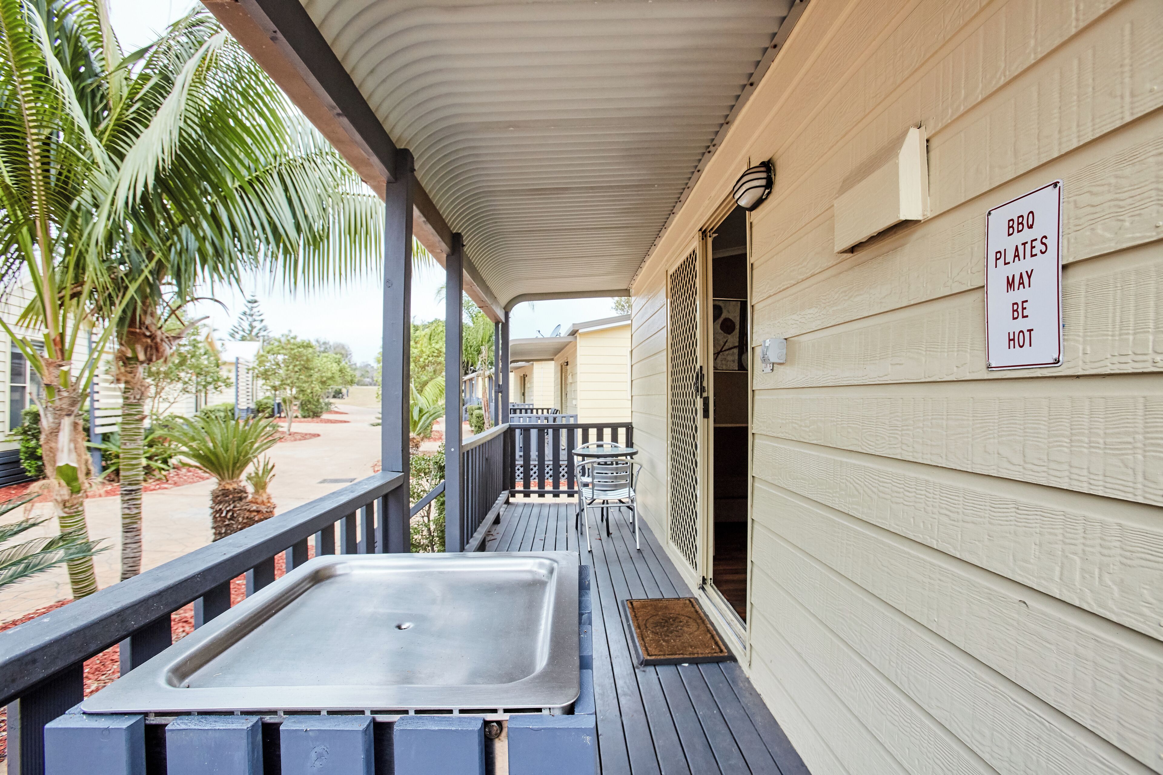 A covered outdoor area with a hot tub, palm trees, and a sign warning about hot plates.