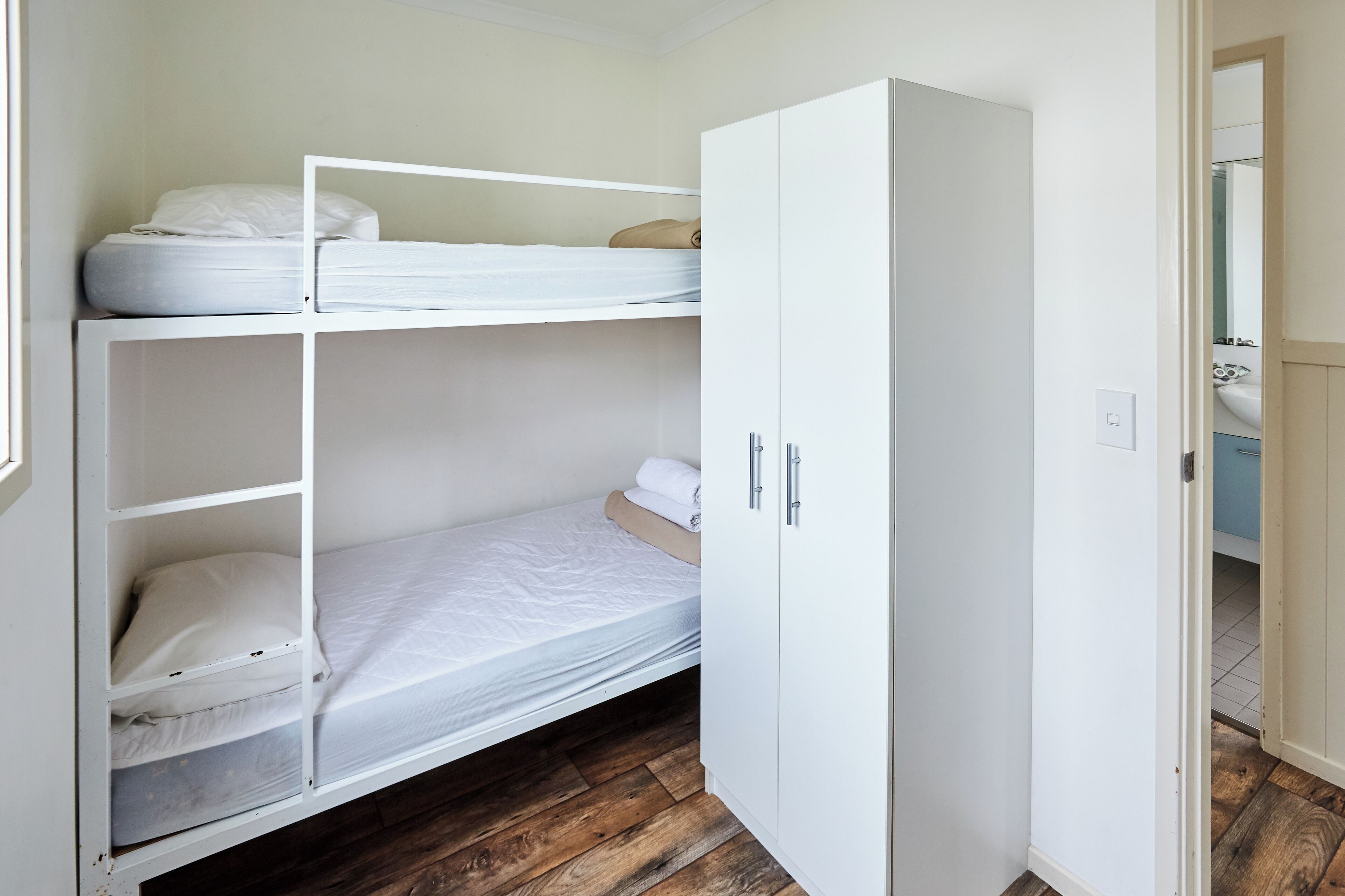 Ein Stockbett mit weißer Bettwäsche, ein Kleiderschrank mit silbernen Griffen und ein Holzboden.