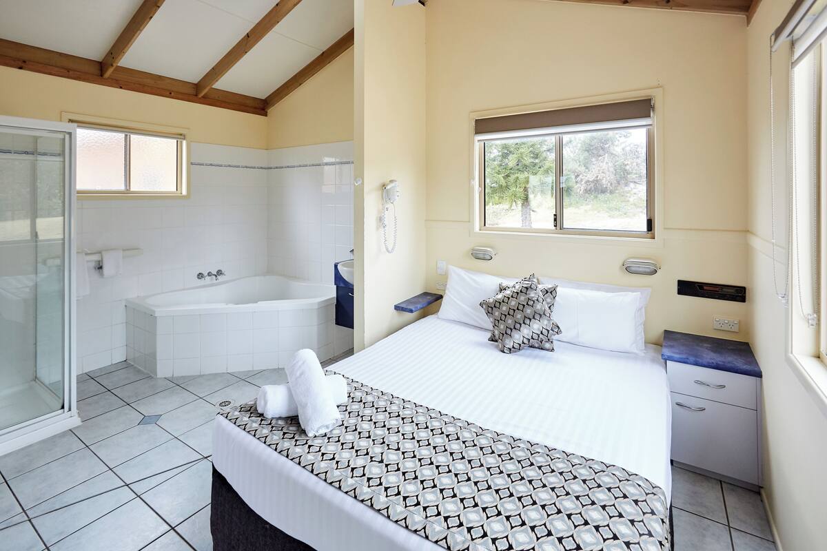 A bedroom with a large bed, a window, a bathtub, and a shower.