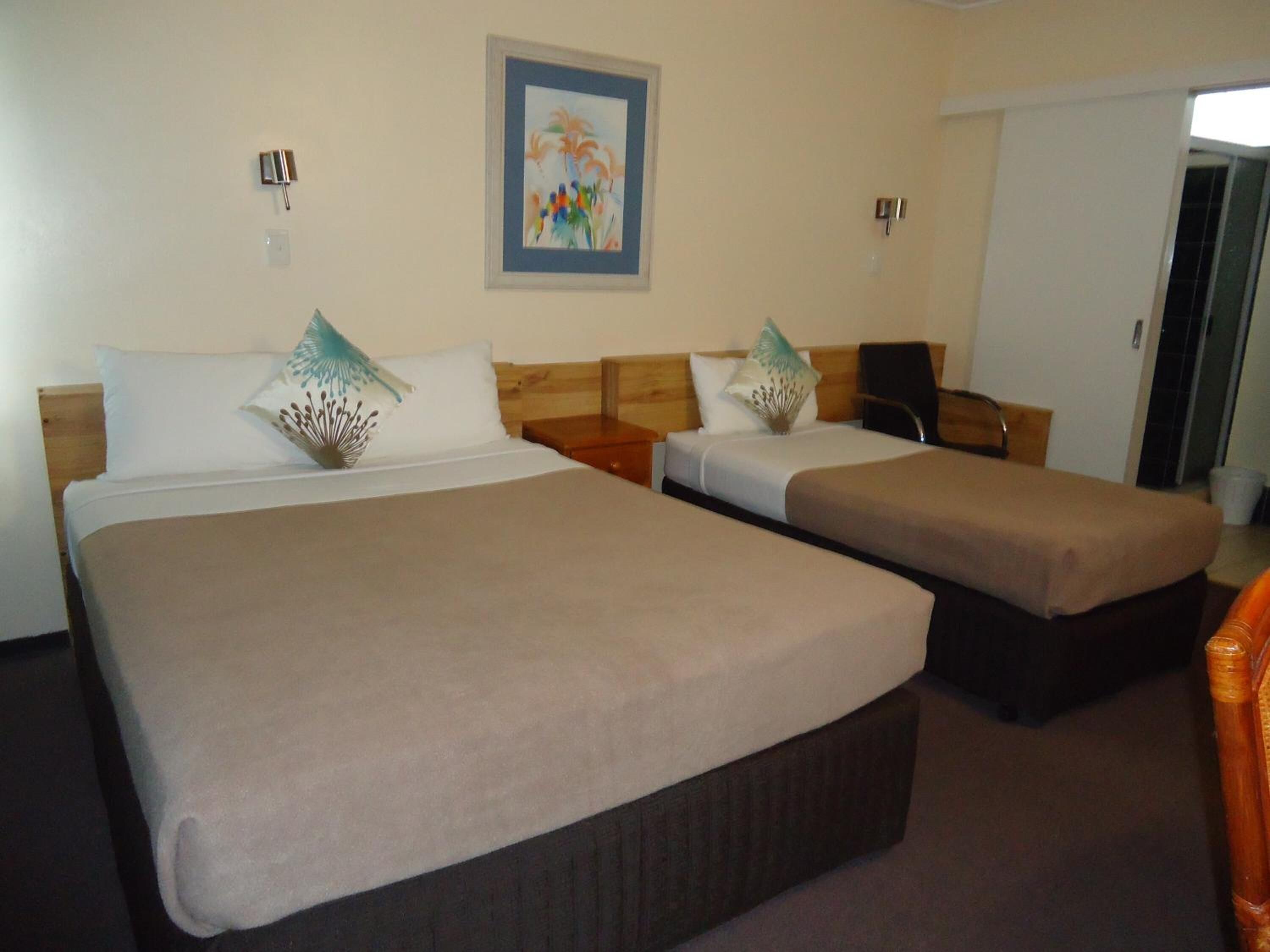 A hotel room with two beds, each with a wooden headboard, a framed picture on the wall, and a small table between the beds.