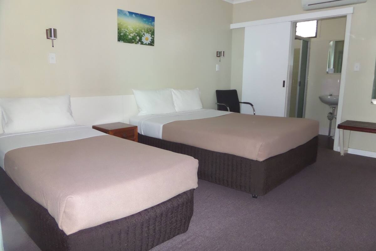 A hotel room with two beds, a desk, a chair, and a bathroom visible through an open door.