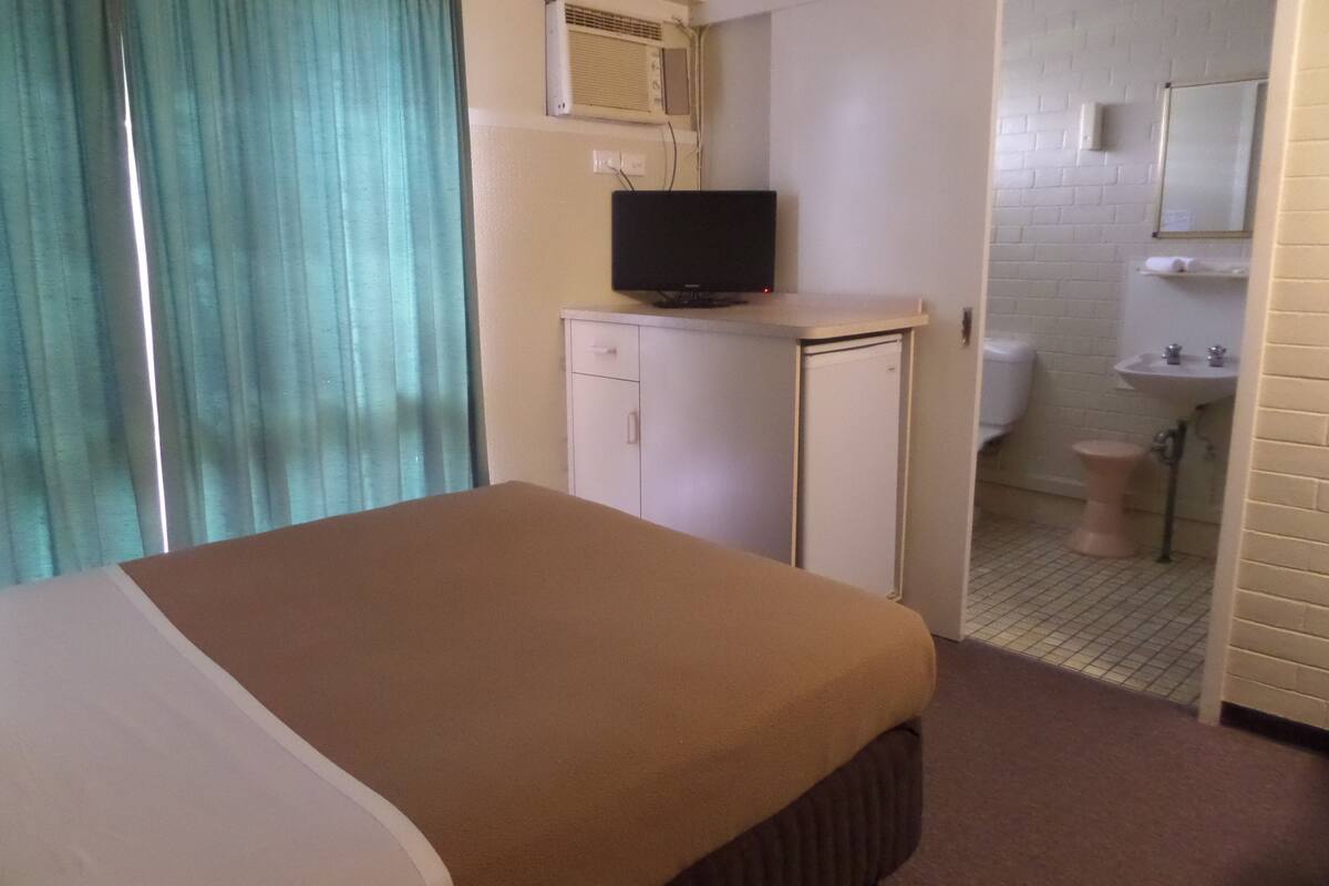A hotel room with a bed, a television on a small table, a bathroom with a toilet and sink, and a mirror on the wall.
