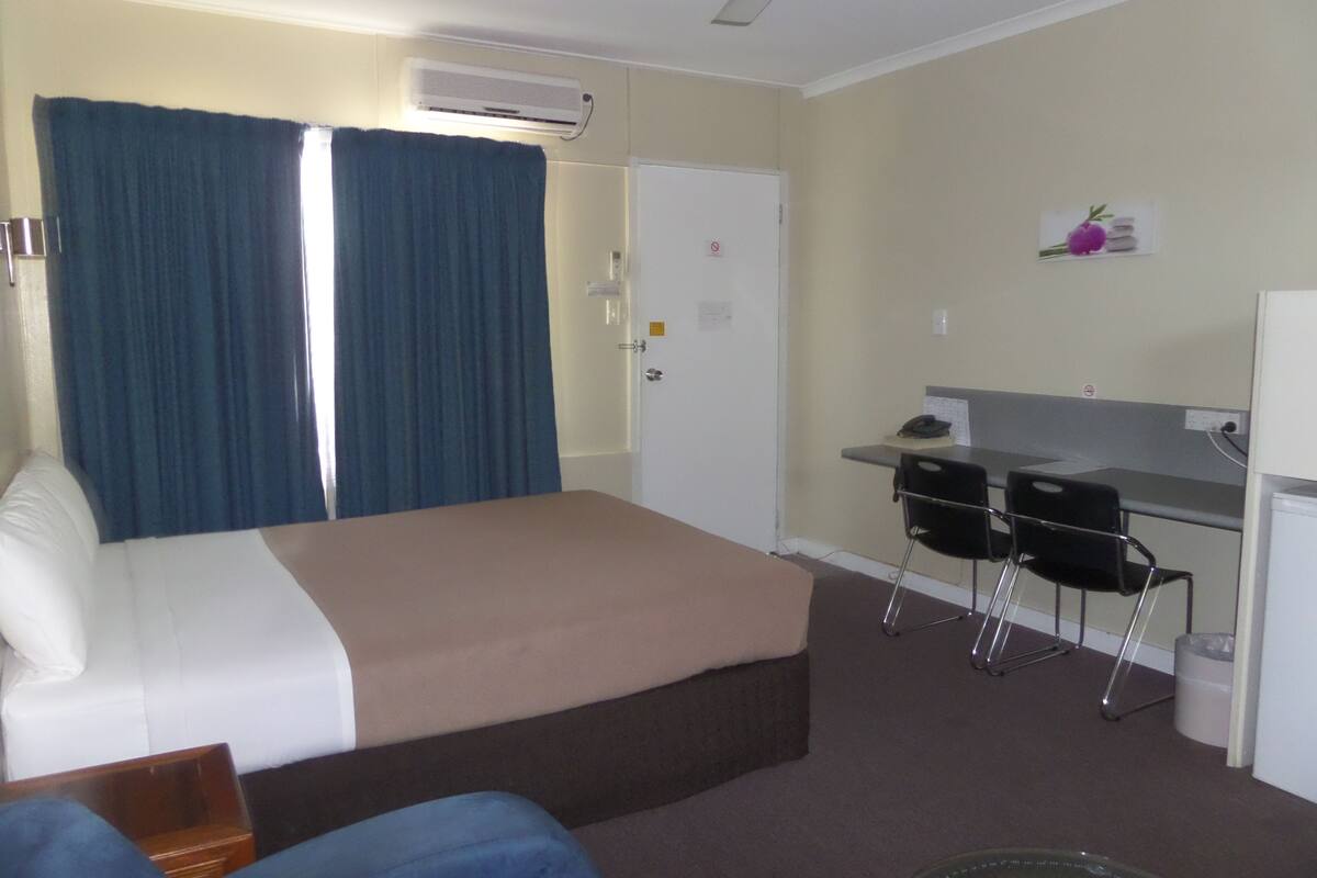 A hotel room with a bed, a desk, two chairs, and a small refrigerator.