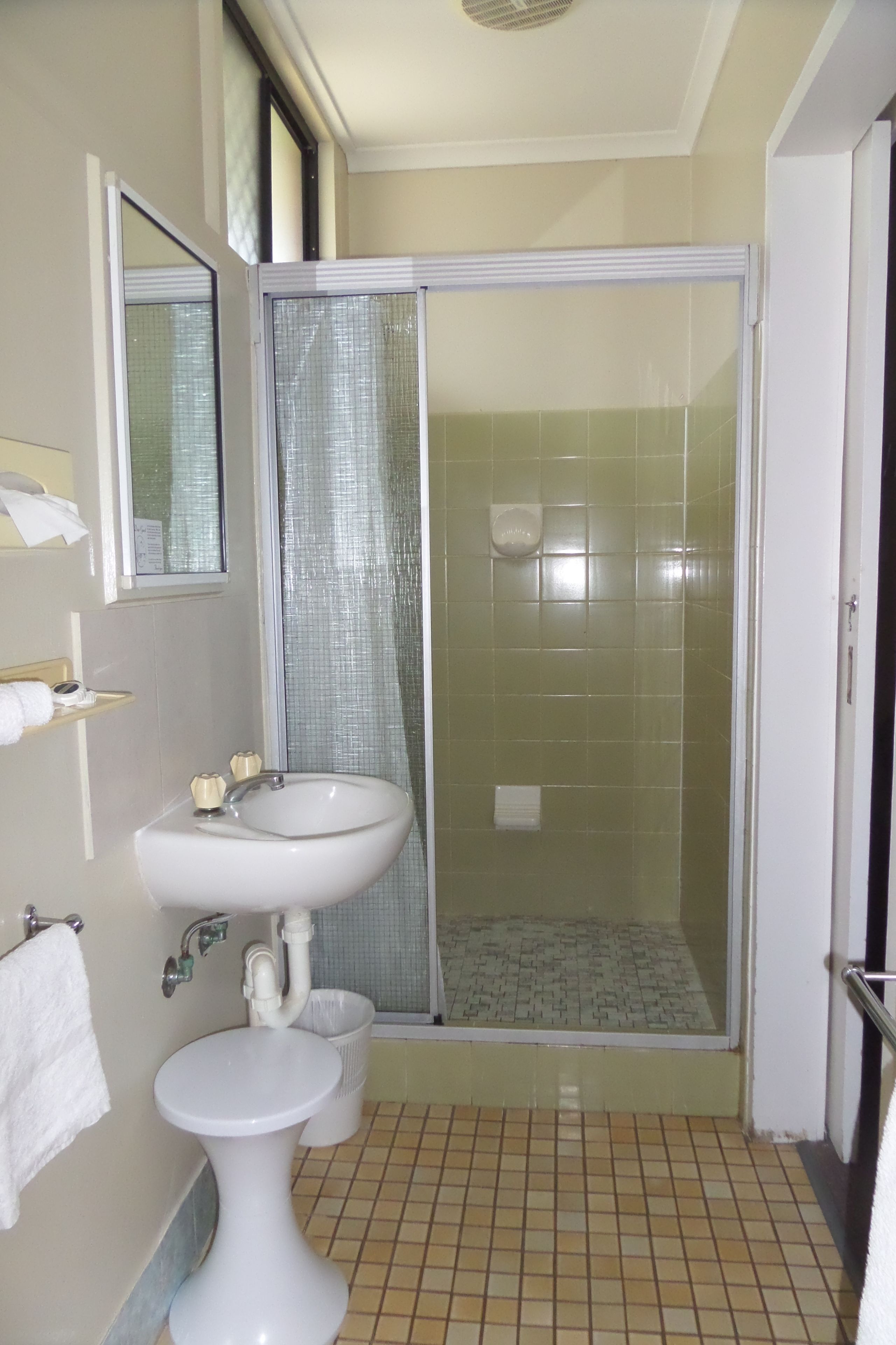 A bathroom with a pedestal sink, a shower with a glass door, and a tiled floor.