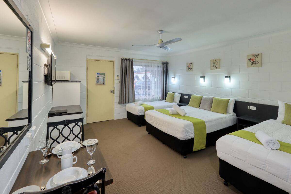 Een hotelkamer met twee bedden, een bureau met stoel, een spiegel en een raam met gordijnen.