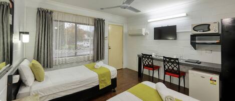 A hotel room with two beds, a desk, a TV, and a refrigerator.