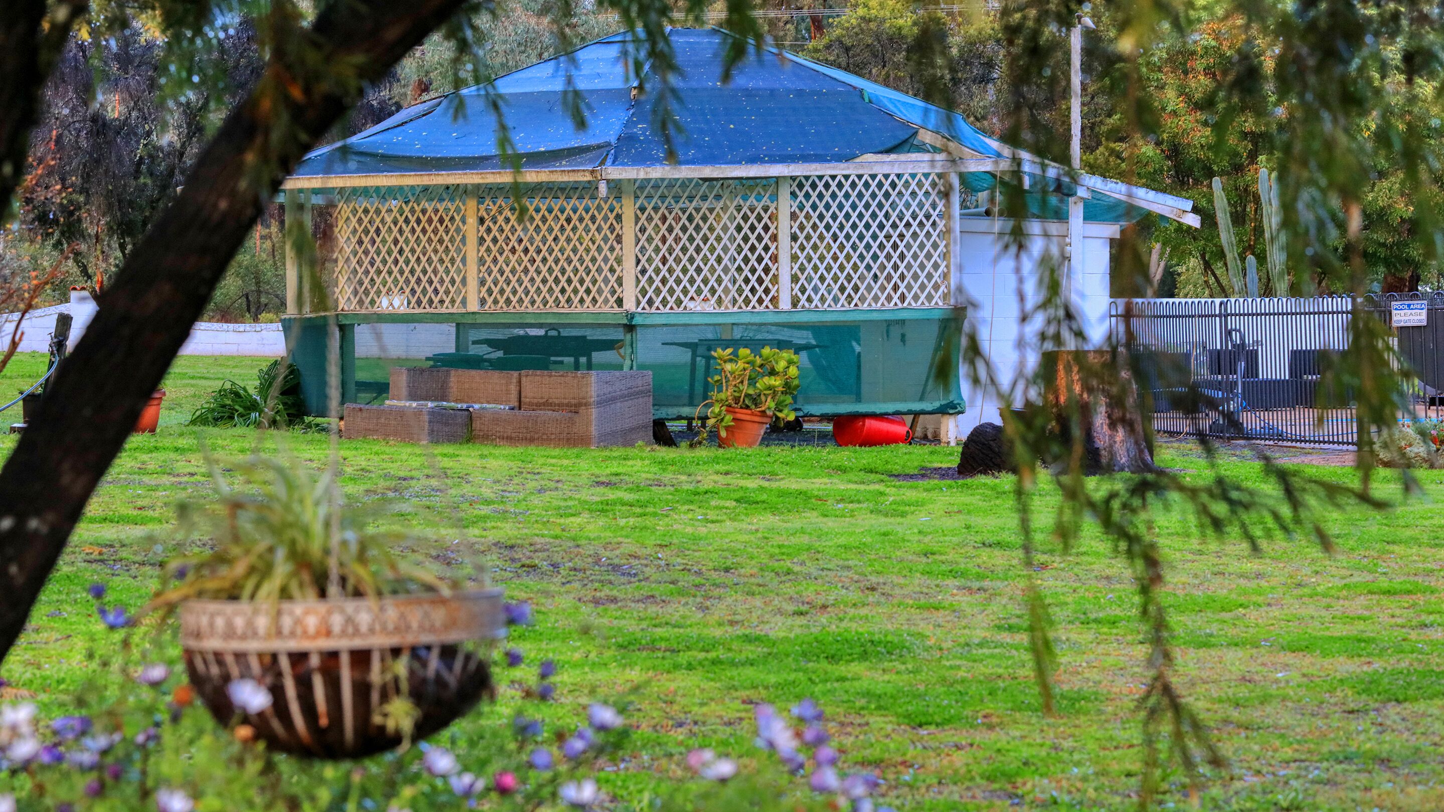 Un espacio al aire libre cubierto con un cerramiento de celosía, plantas en macetas y una zona de piscina con un cartel.