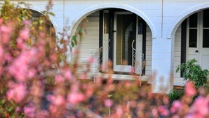 Un edificio con tres ventanas arqueadas y una puerta, rodeado de flores en flor.
