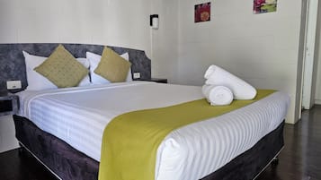 Een netjes opgemaakt bed met een wit-groene spreideken, een donker hoofdbord en twee kussens.