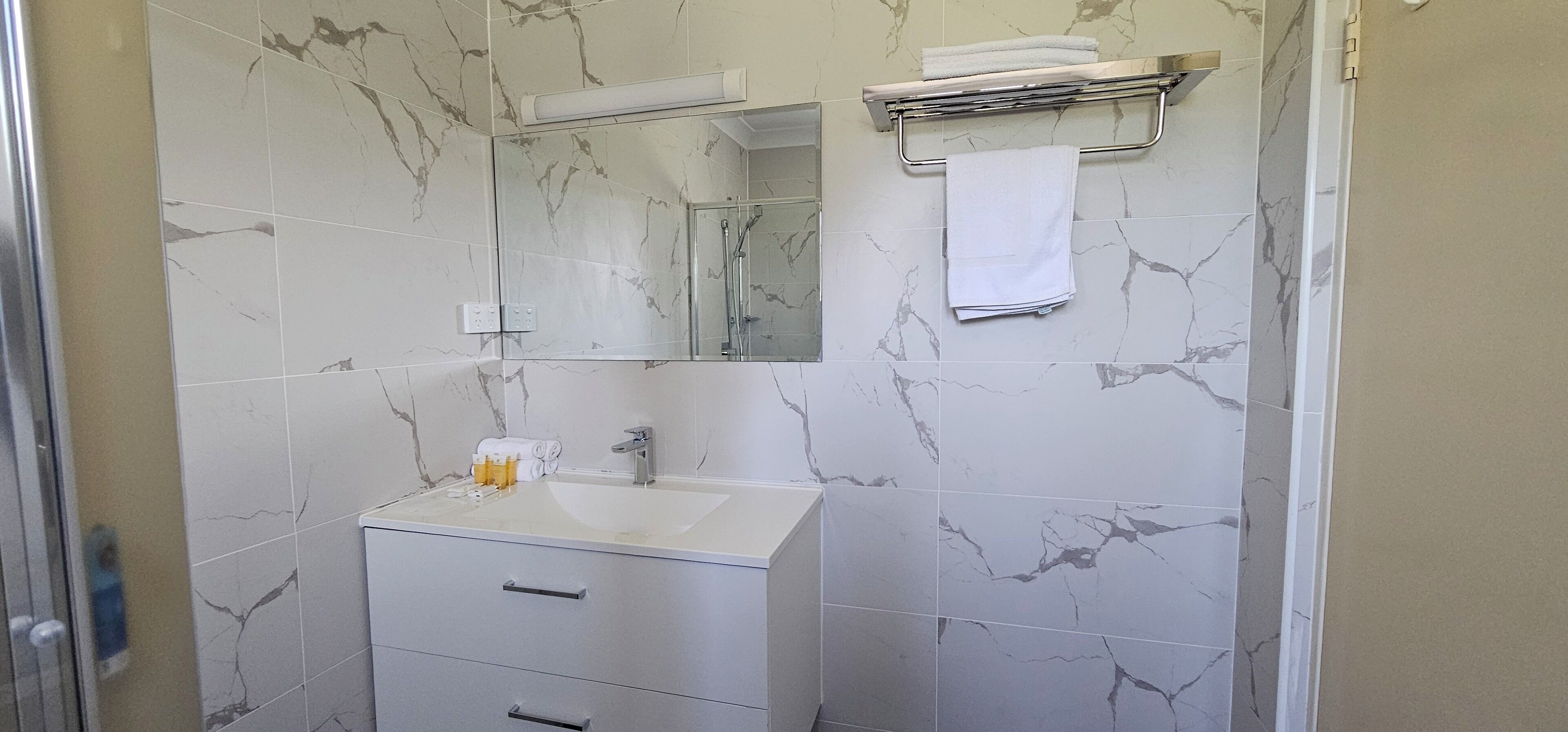 Un baño con lavamanos blanco, espejo y paredes con diseño de mármol.