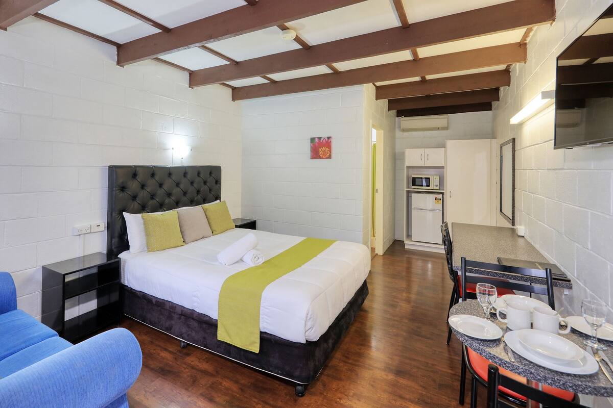 Een hotelkamer met een bed, een klein tafeltje met borden en glazen, een magnetron en een koelkast.