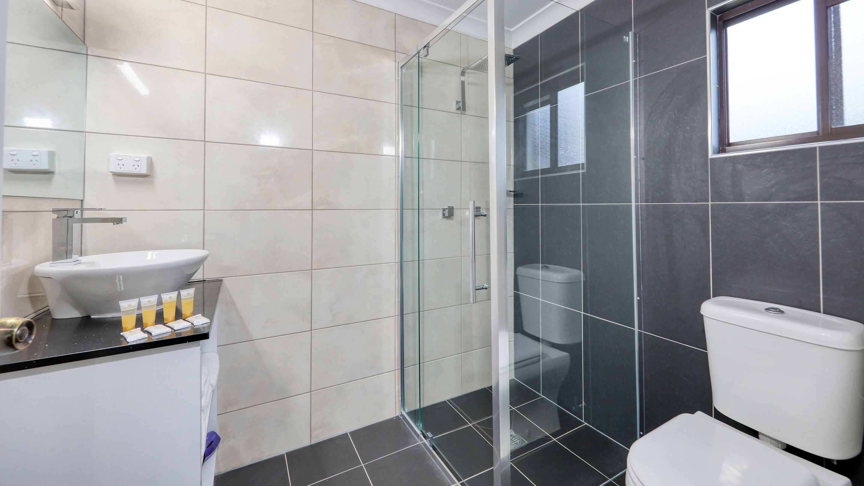 A modern bathroom with a glass-enclosed shower, a white sink with toiletries, and a toilet.