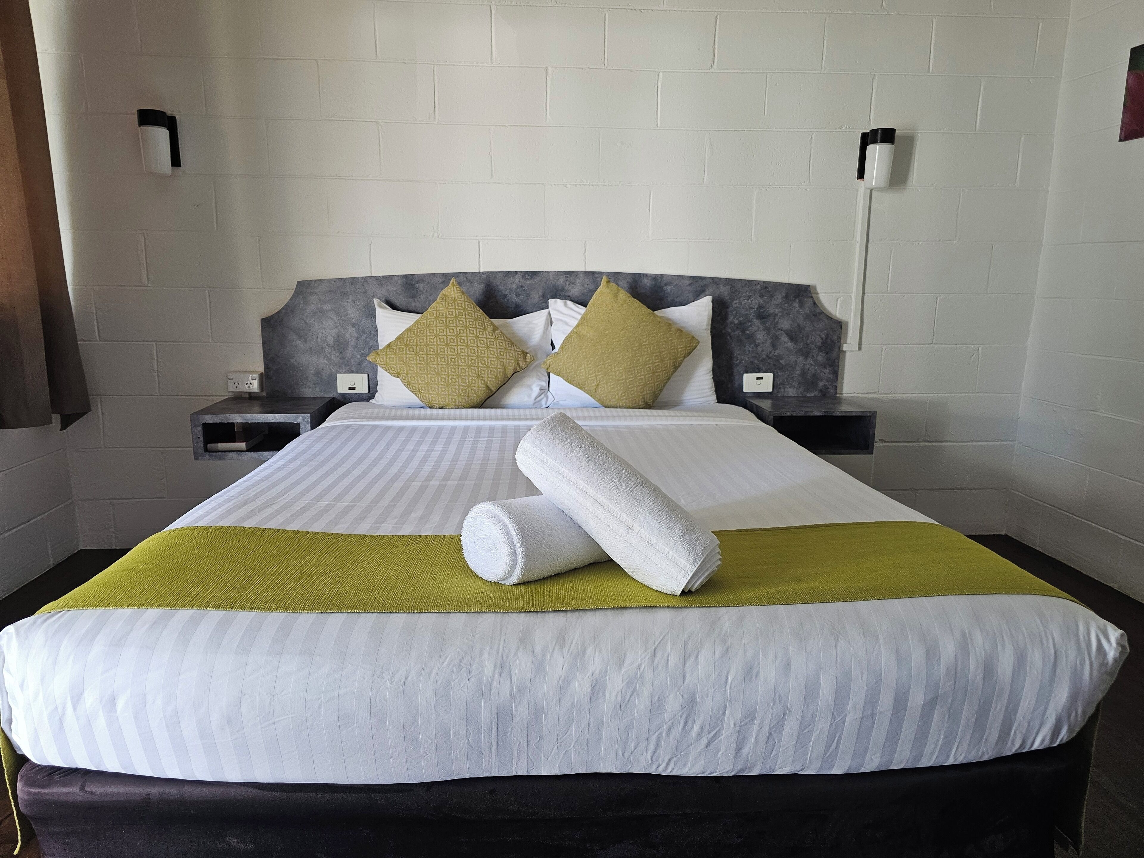 Ein ordentlich bezogenes Bett mit einer weiß-grünen Streifenauflage, zwei Kissen und einem aufgerollten weißen Handtuch.