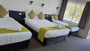Habitación de hotel con tres camas individuales, cada una con cubrecama verde y almohadas blancas.
