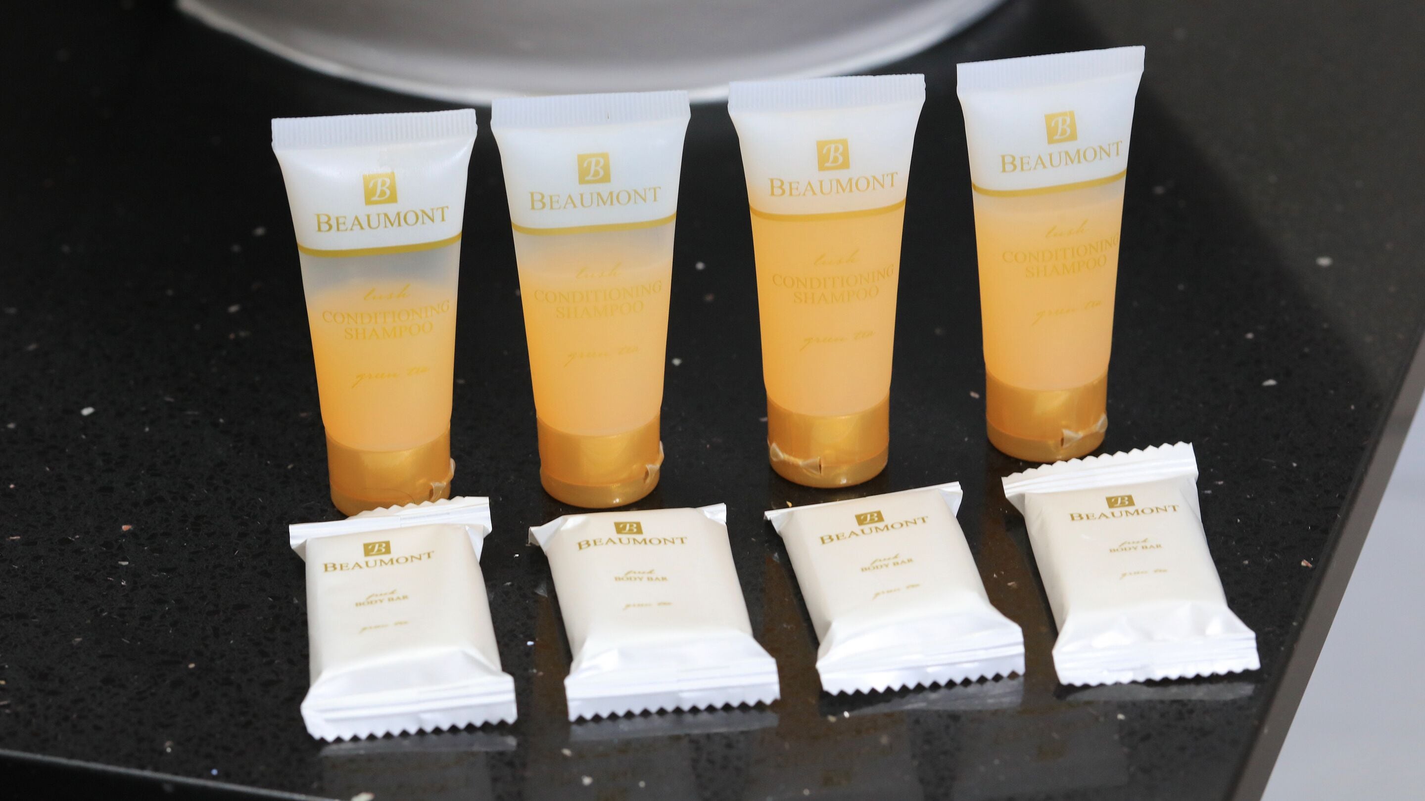 Vier tubes Beaumont conditioner shampoo en vier zakjes Beaumont body soap op een zwart aanrecht.