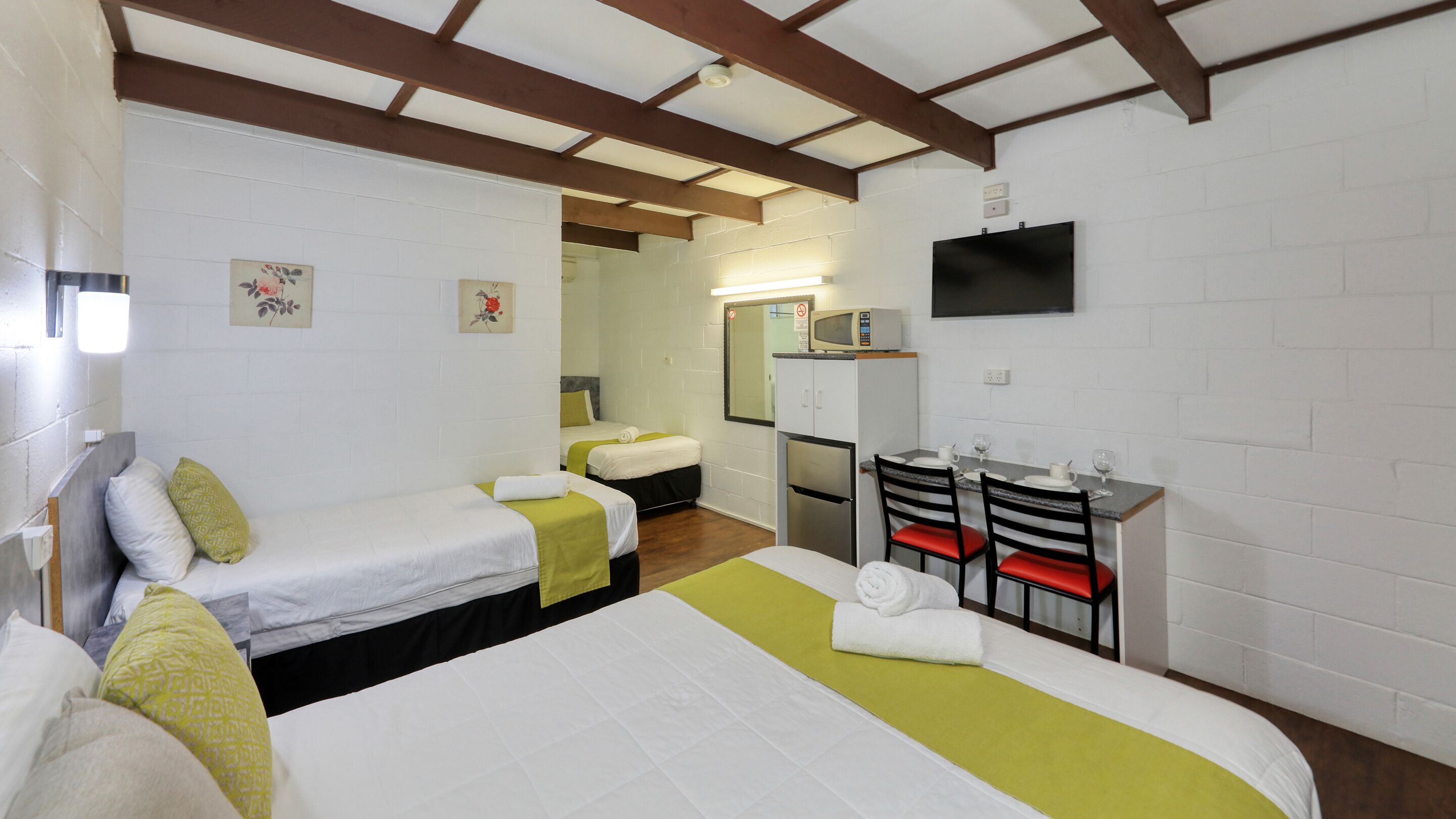 A hotel room with two single beds, a small kitchenette, a TV, and a mirror.
