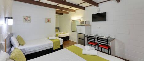 A hotel room with two single beds, a small kitchenette, a TV, and a mirror.
