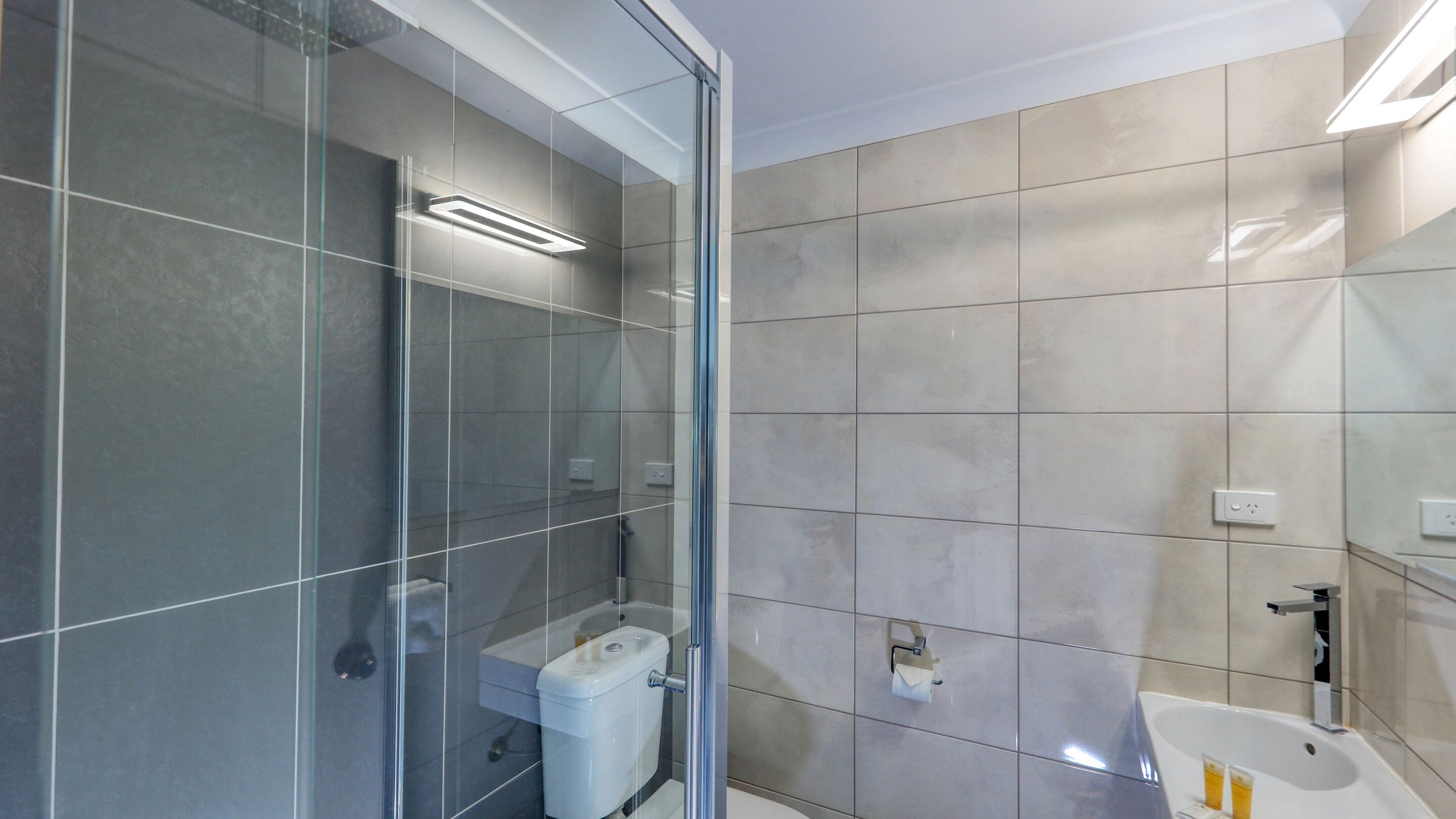 Et moderne badeværelse med brusekabine i glas, toilet og vask.