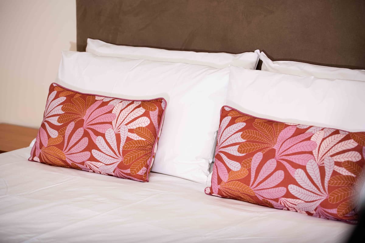 Una cama con ropa blanca y dos almohadones decorativos con diseño de hojas.