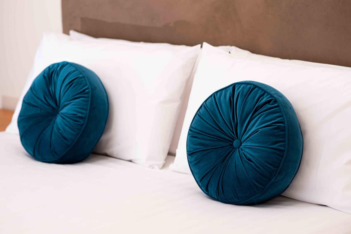 Una cama con dos almohadas turquesa y ropa de cama blanca.