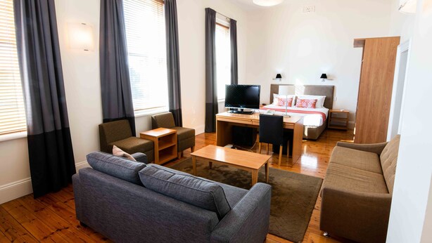 Un salon moderne avec un canapé gris, une table basse en bois, un téléviseur et un bureau avec une chaise.