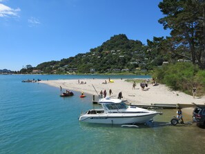 A beach with a boat docked near the shore, people on the sand, and houses in the background. - Ocean Breeze Resort (Pauanui)