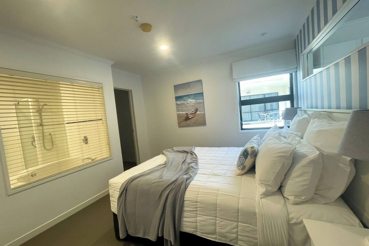 Quarto com cama, janela com persianas, um quadro e uma luminária no teto.
