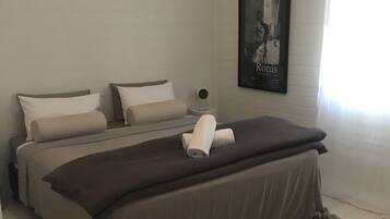 A bedroom with two beds, a framed picture on the wall, and a window with curtains.