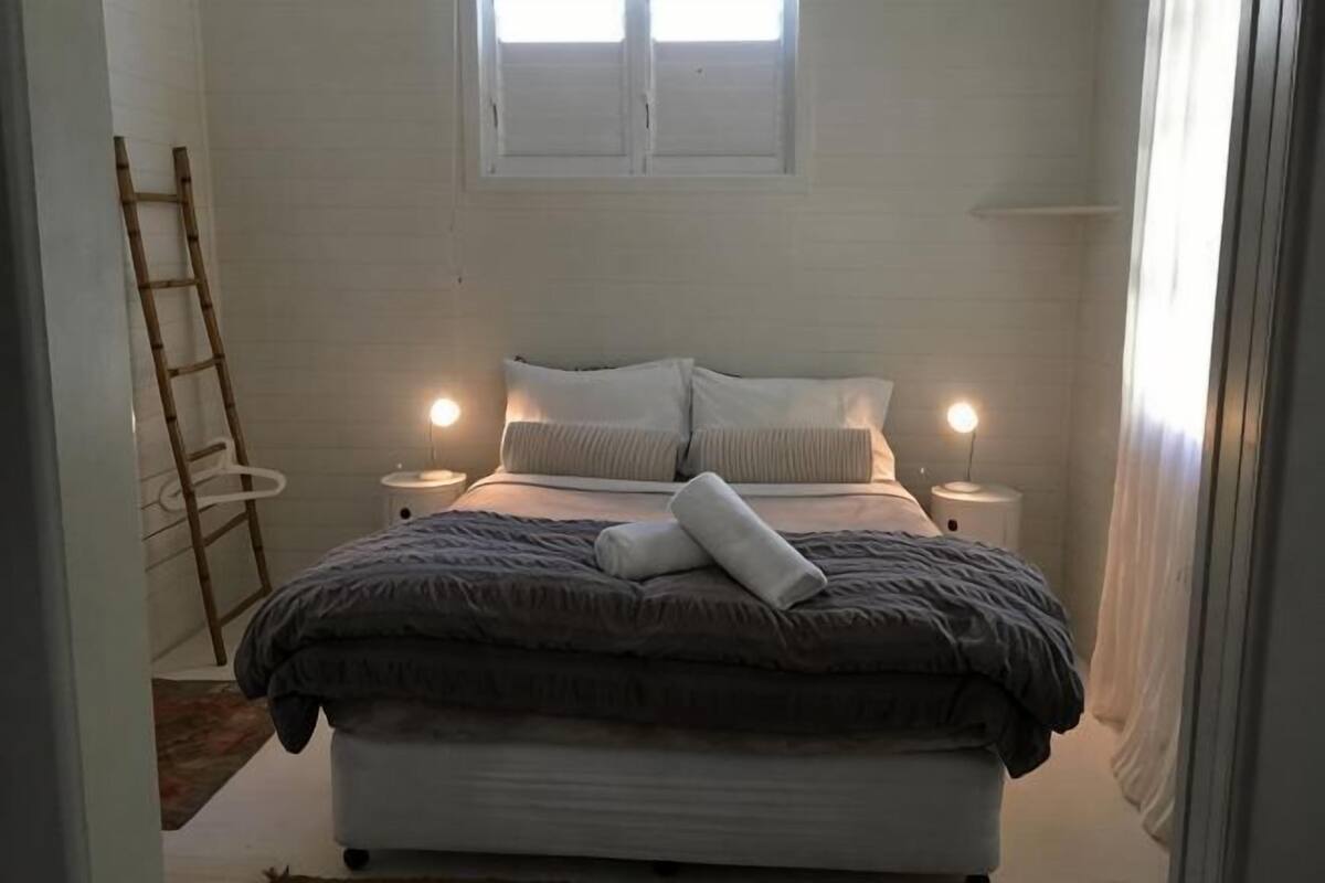 A bedroom with a bed, bedside lamps, a ladder, and a window.
