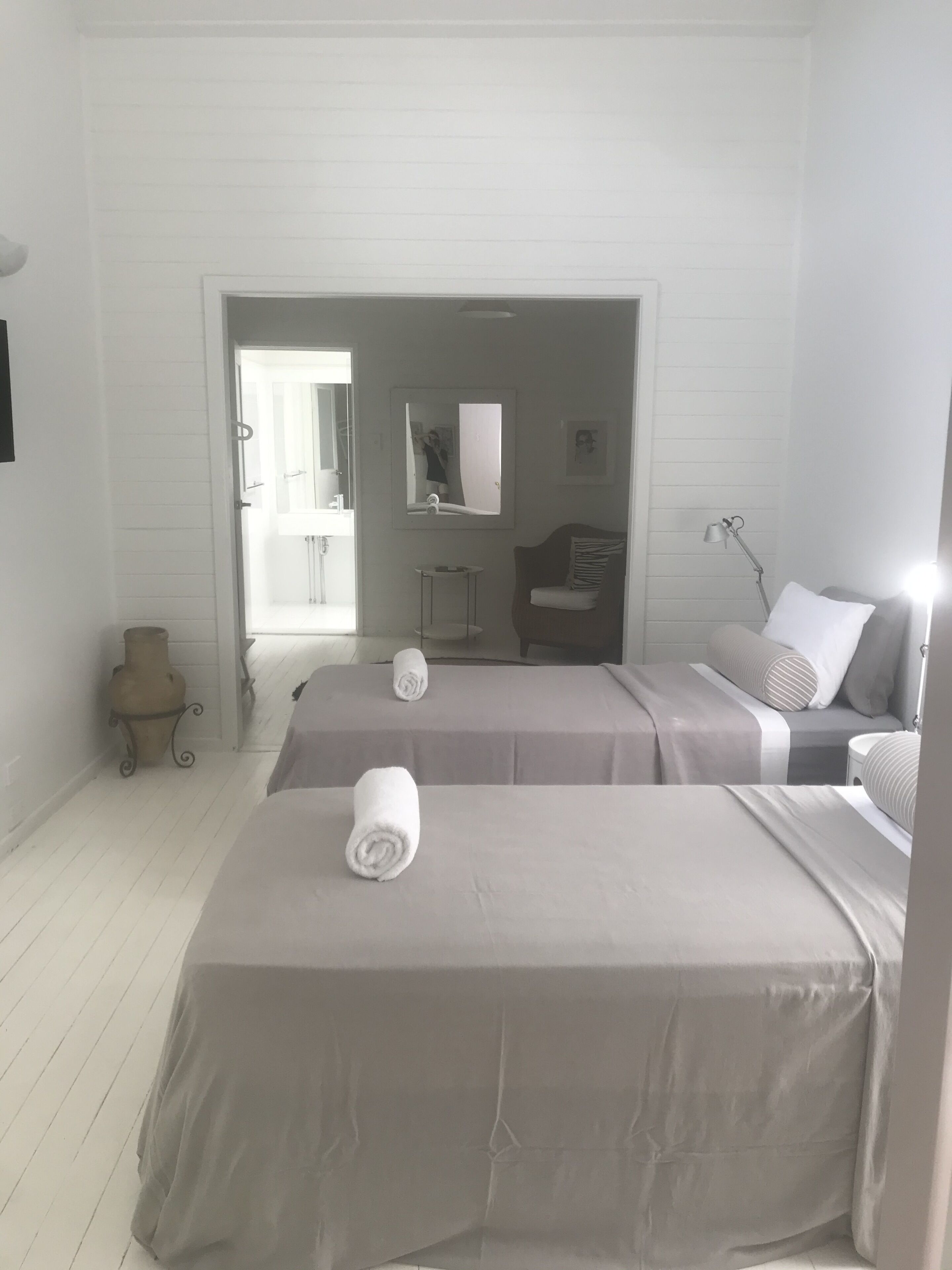 A hotel room with two beds, a small table, a mirror, and a door leading to a bathroom.