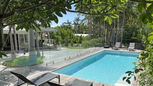 A rectangular swimming pool with a wooden deck, surrounded by lounge chairs and a covered seating area. - Byron Springs (Byron Bay)