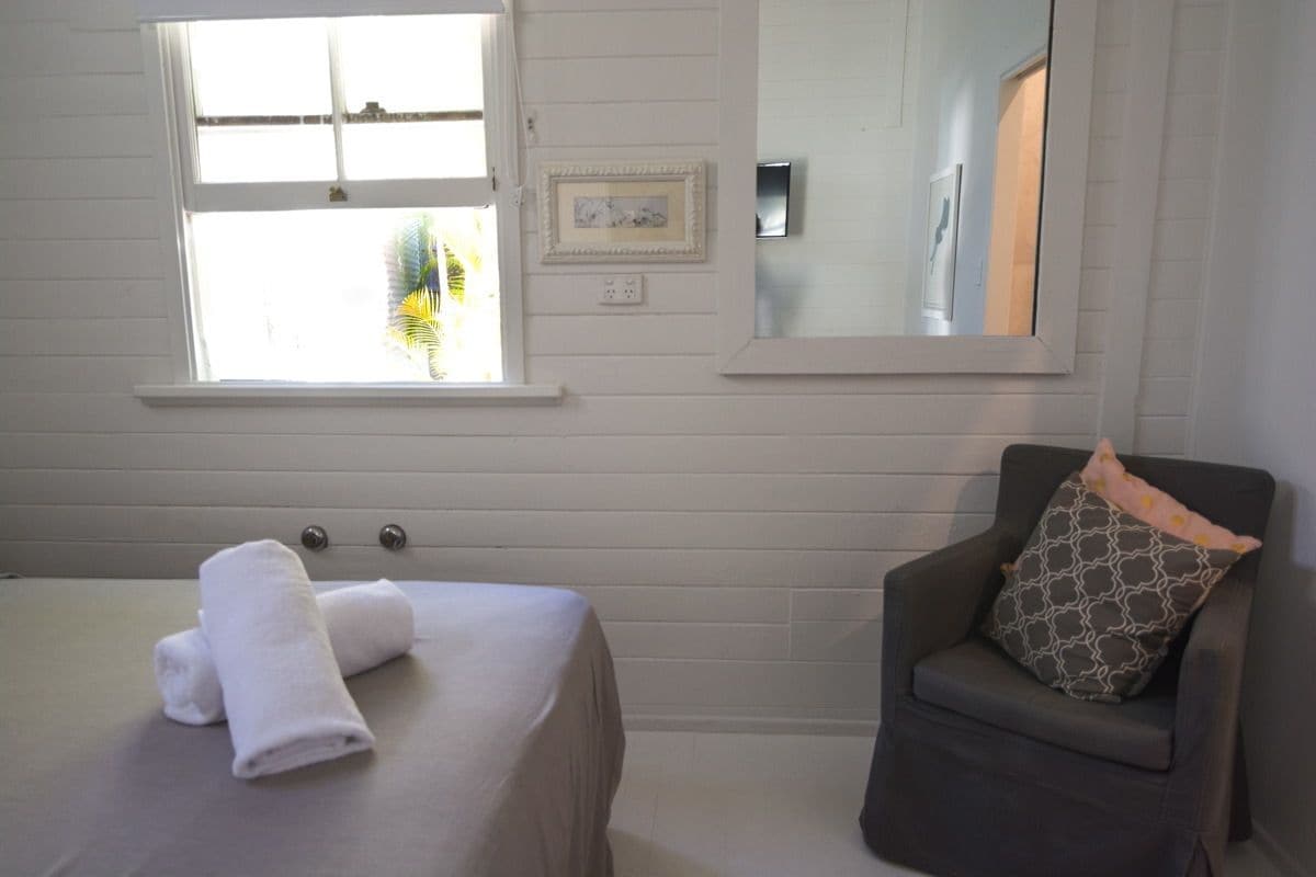 Una habitación con cama, una silla, un ventanal y un espejo.