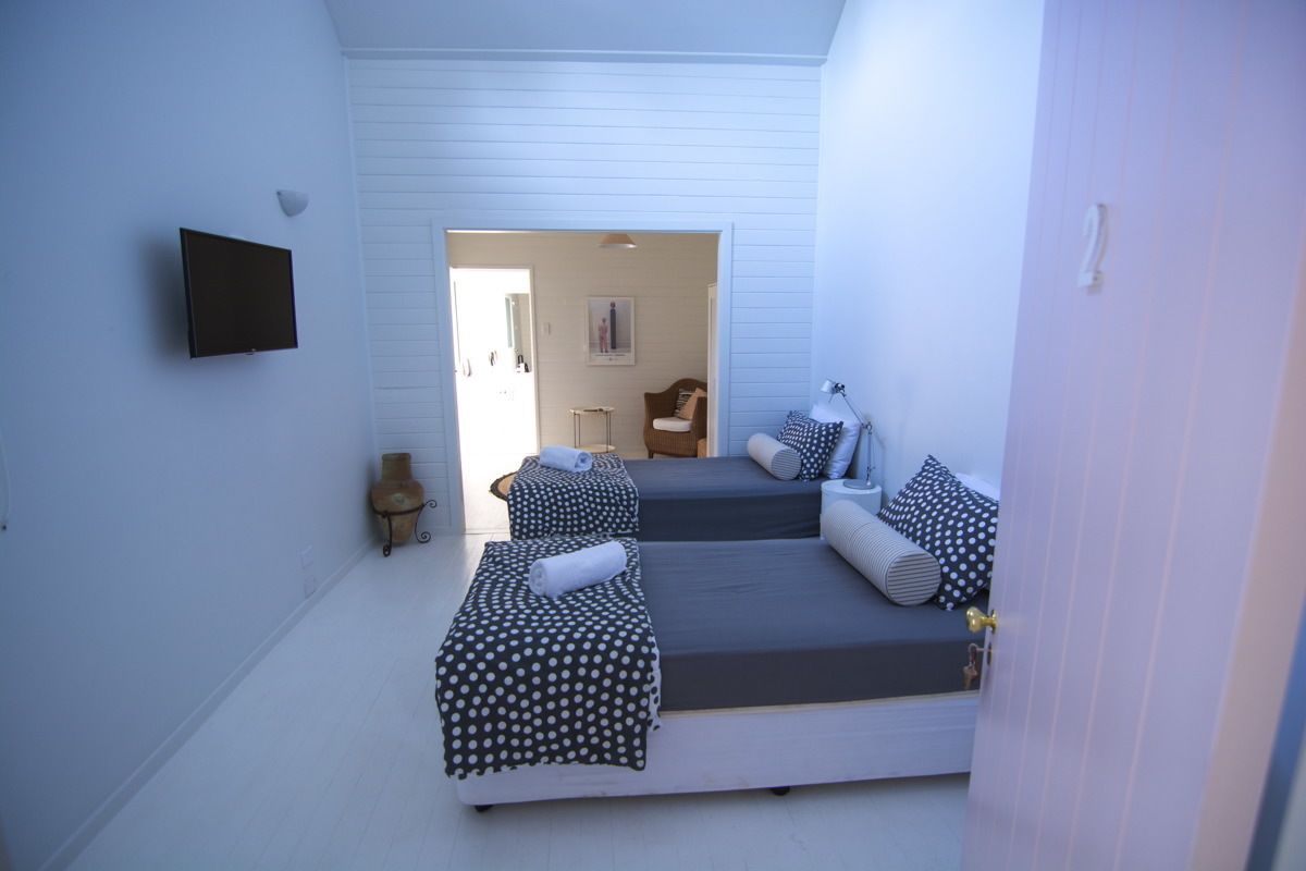 Una habitación con dos camas, un televisor de pantalla plana montado en la pared y una pequeña mesa con lámpara.