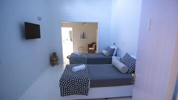 Una habitación con dos camas, un televisor de pantalla plana montado en la pared y una pequeña mesa con lámpara.