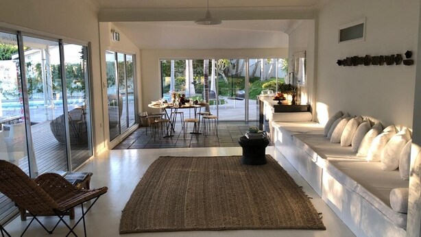 A spacious living area with a large window, a sofa, a dining table, and a wicker chair. - Byron Springs (Byron Bay)
