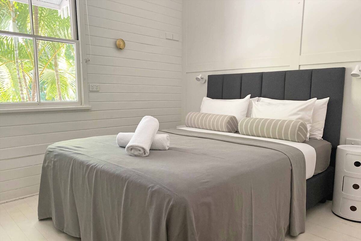 A neatly made bed with a grey bedspread, two rolled white towels, and striped pillows.