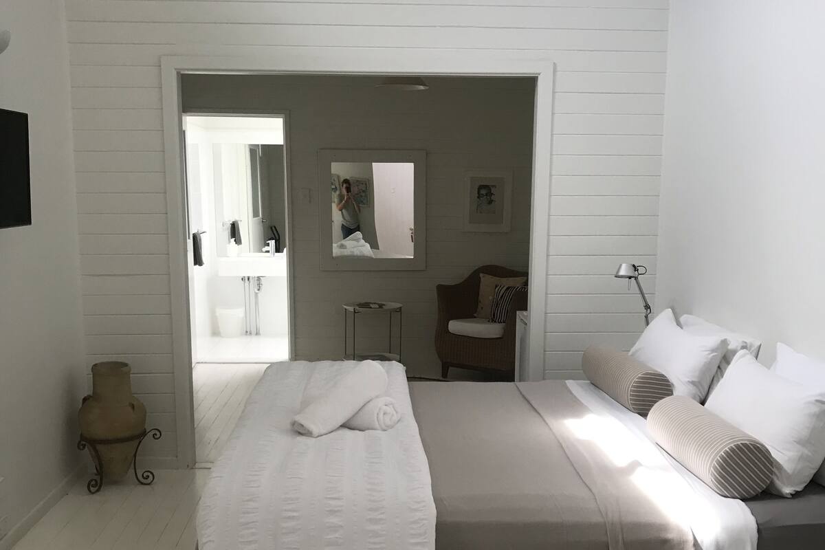 A bedroom with a large bed, a bedside table, a lamp, a mirror, and a view into the bathroom.