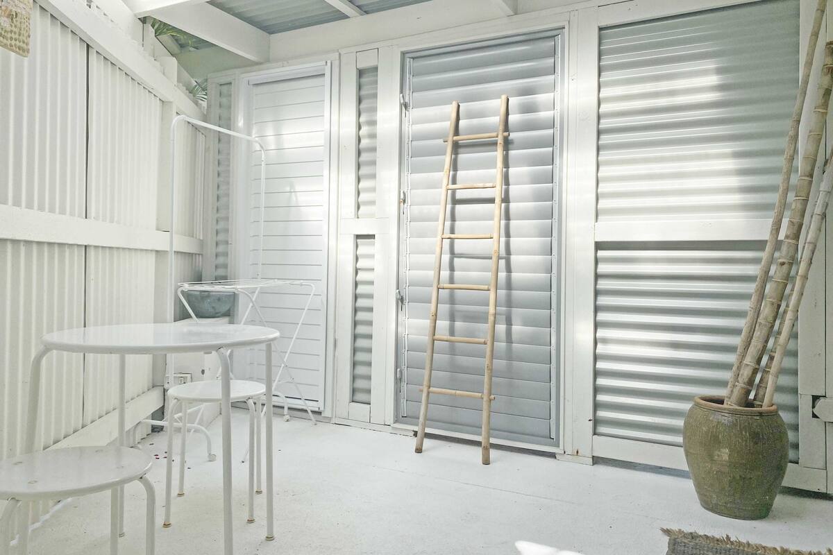A white interior space with a table and chairs, a ladder leaning against a door, and a potted plant.