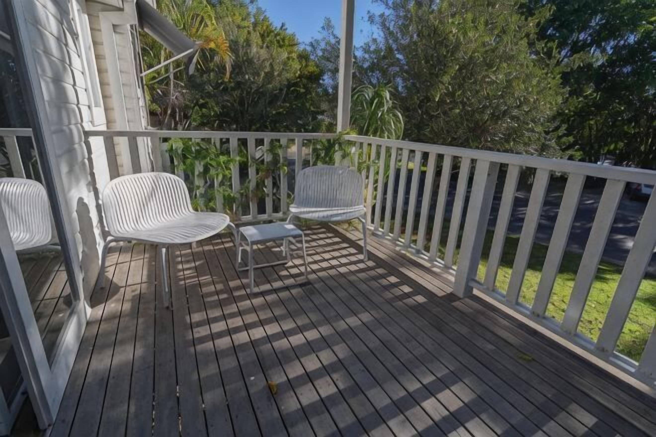 A wooden deck with white railings, two white chairs, and a small table.