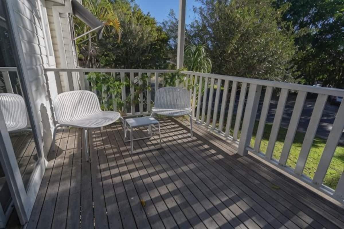 A wooden deck with white railings, two white chairs, and a small table.